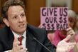 A protester holds a sign behind Geithner as he addresses a hearing of the Congressional Oversight Panel of the TARP.